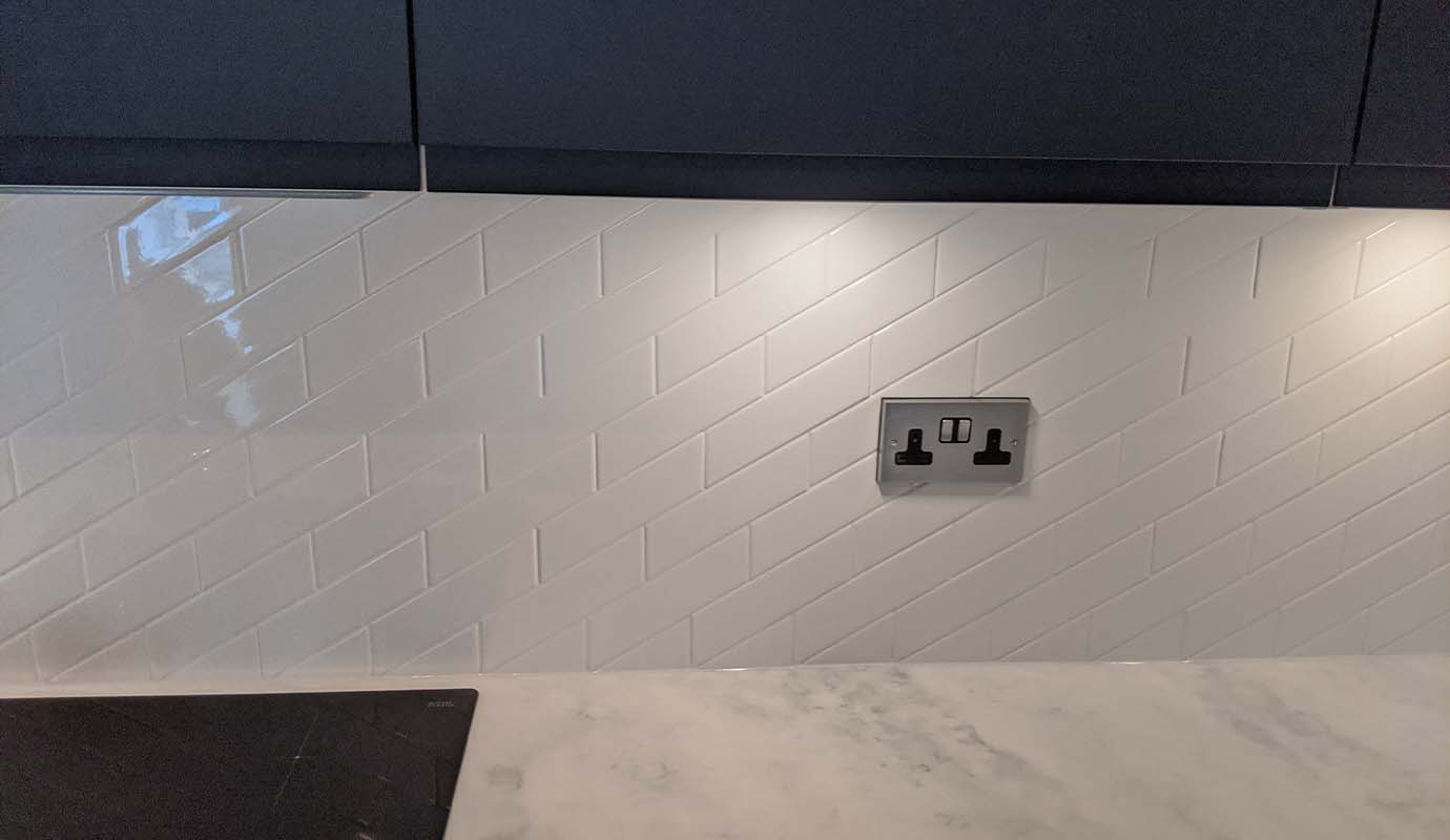 A modern kitchen with herringbone tile backsplash, marble countertop, and a UK style power socket.