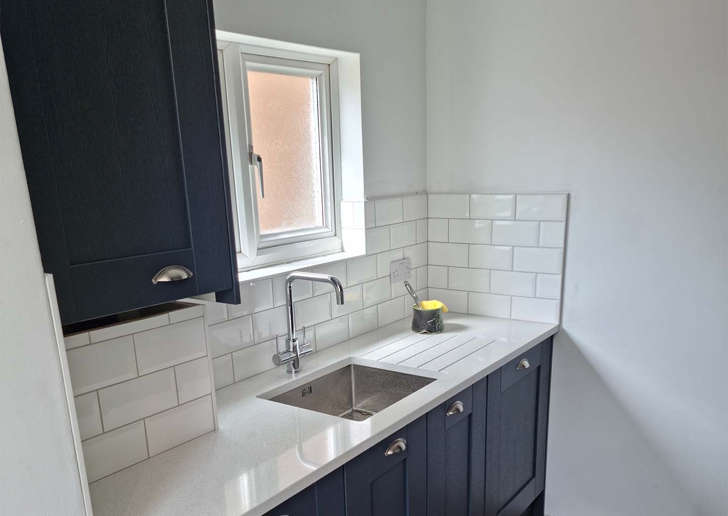 A modern kitchen corner with a sink, frosted window, and dark cabinets.