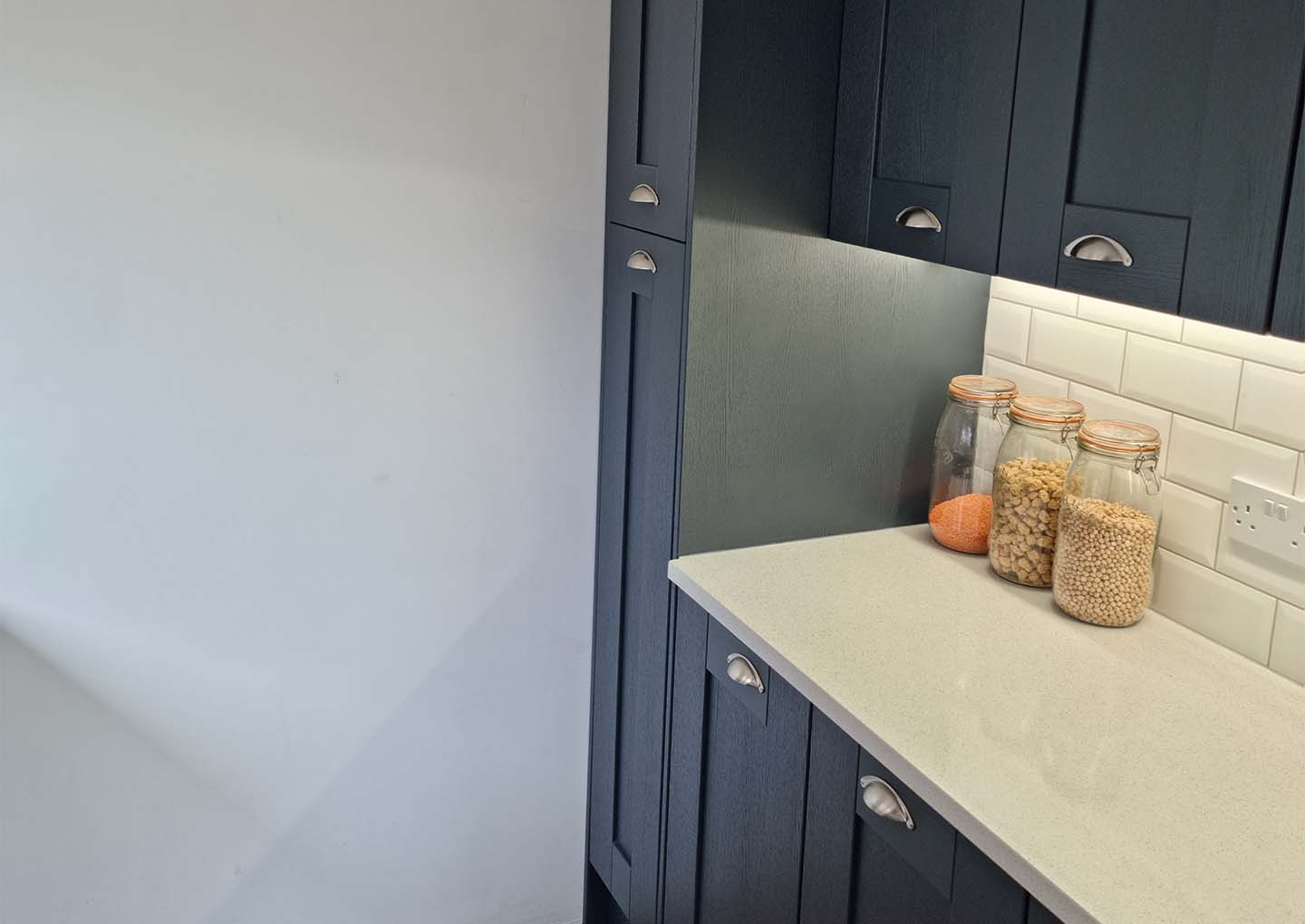 Modern kitchen corner with dark cabinetry and jars on countertop.