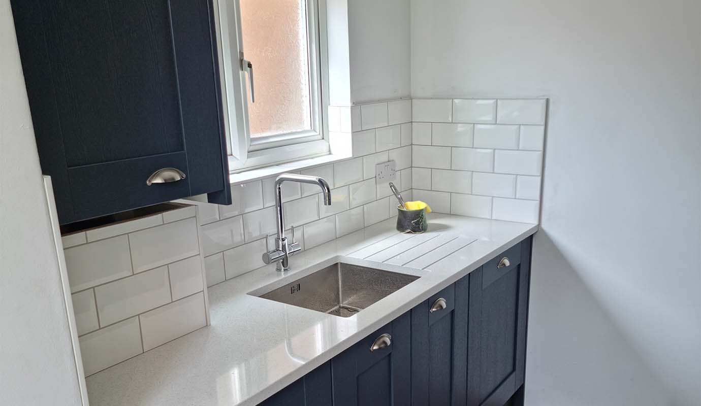 A modern kitchen corner with a sink, frosted window, and dark cabinets.