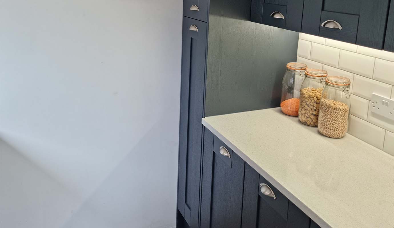 Modern kitchen corner with dark cabinetry and jars on countertop.