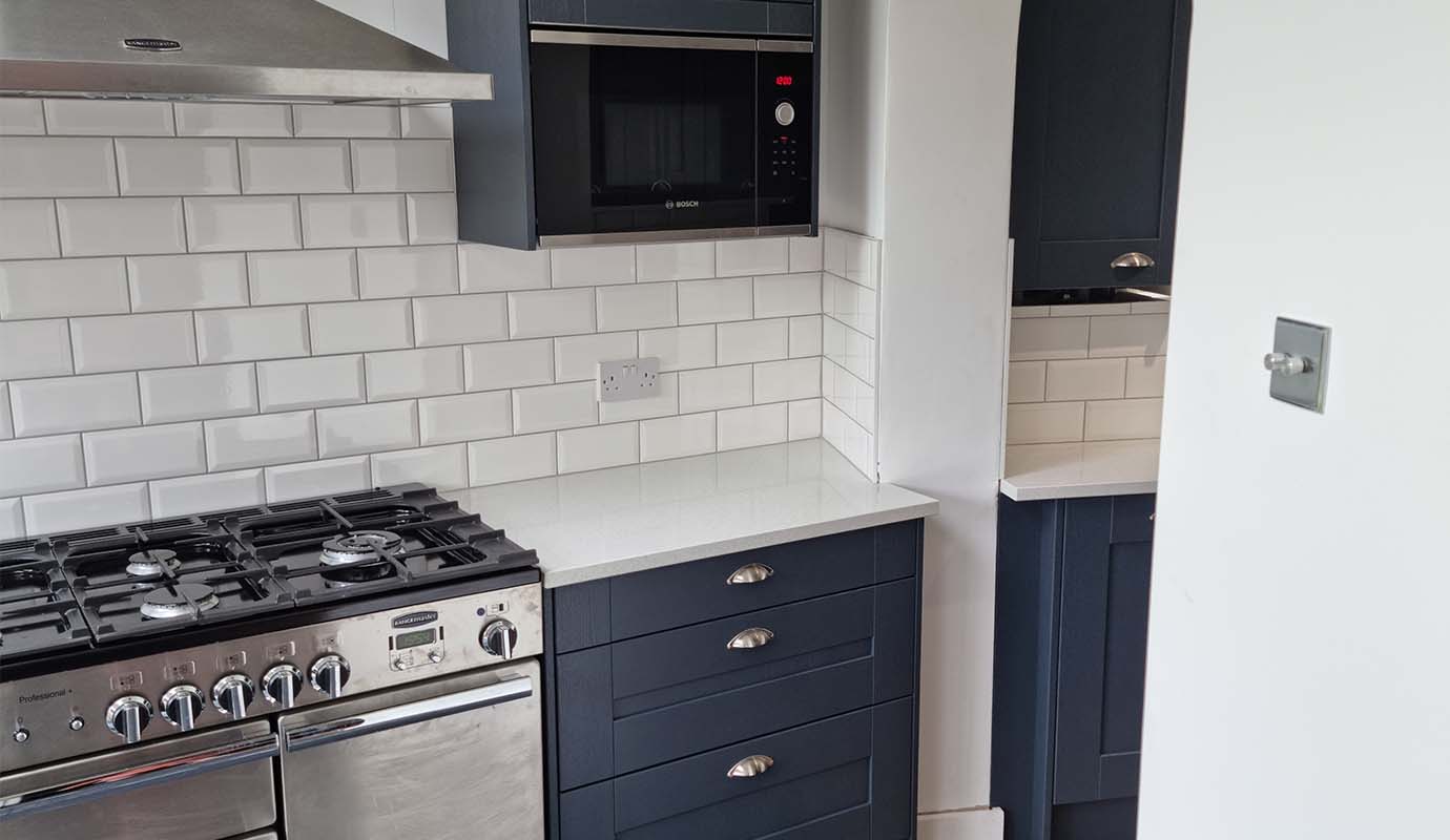 Modern kitchen corner with stainless steel stove, microwave, and white subway tiles.
