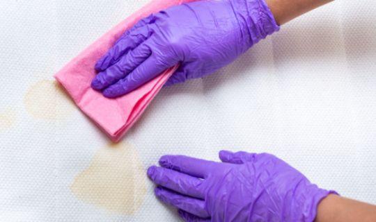 a professional's hands wearing blue gloves cleaning a mattress