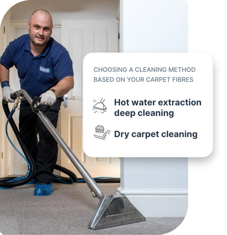 A carpet cleaning technician who is wearing a dark blue Fantastic Services uniform and using a hot water extraction machine to deep clean a wall-to-wall carpet.