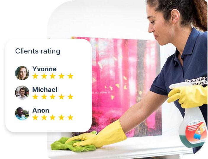 A cleaner who is wearing a dark blue Fantastic Services uniform and yellow latex gloves. She is holding a spray bottle with detergent and using a green wiping cloth to clean a shelf within an apartment. The picture is edited, showing a segment with 5-star ratings from customers.