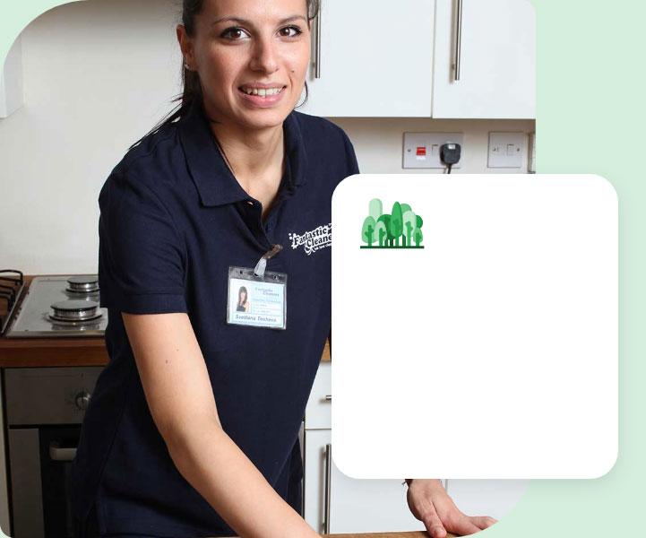 A professional cleaner wearing a dark blue Fantastic Services uniform and an ID badge. She is using a blue cloth to wipe the countertop next to a kitchen sink.