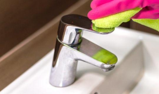 a professional cleaner's hand wearing a globe scrubbing a chrome tap