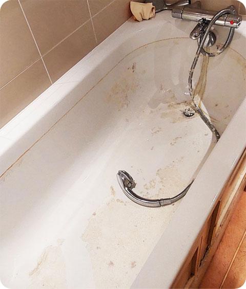An image of a bathtub covered in dirt and grime. The tub's surface is stained and discolored, with soap scum and dirt visible along the edges. The drain is clogged with hair and debris, and there are watermarks on the walls and floor surrounding the tub. Overall, the bathtub appears neglected and in need of a thorough cleaning.