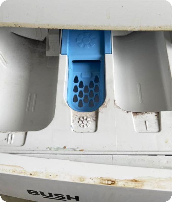 An image of a dirty dishwasher detergent compartment, showing visible residue, grime, and buildup. The detergent compartment appears caked with dried soap residue, food debris, and hard water stains. The compartment looks neglected and in need of thorough cleaning to remove the accumulated dirt and restore its functionality.