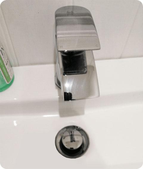 A close-up shot of the same white porcelain bathroom sink with a chrome faucet and drain. The sink has been cleaned meticulously, and the faucet and drain have been thoroughly descaled and polished.