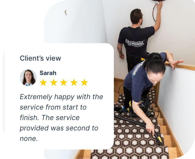 The image shows a couple of Fantastic Services tenancy cleaners who are on the job. They are cleaning a carpeted stairway. One of the cleaners is hoovering the carpeted area while the other is removing smudges from the wall.