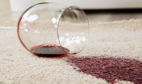 a wine glass next to a wine stain on a carpet