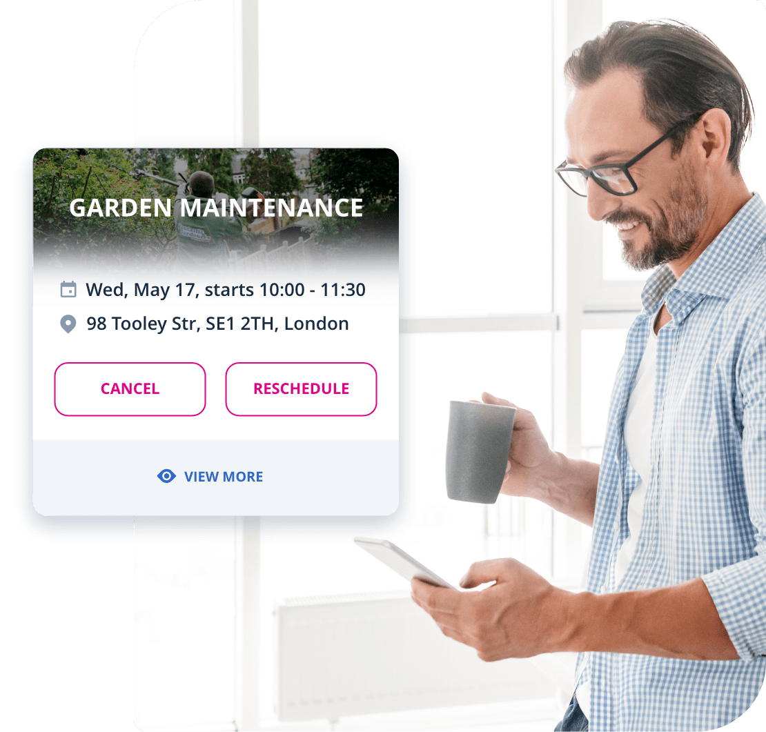 The image shows a Fantastic Services customer who is standing in a brightly lit room next to a window. He is holding his smartphone and looking at the screen, arranging his garden maintenance service with Fantastic Services.