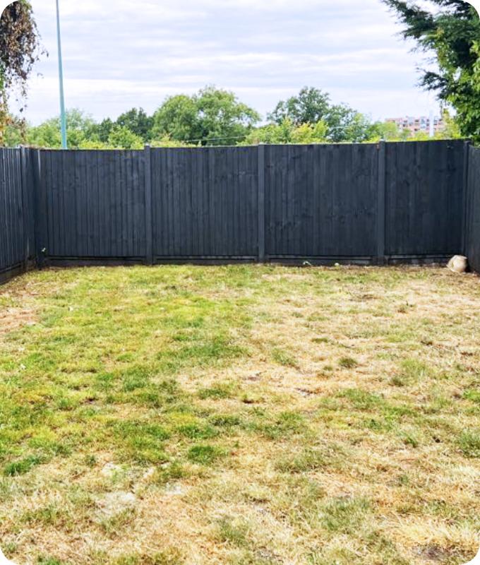 The image shows the same backyard with a black wooden fence. It has been cleared of overgrowth and it looks much neater.