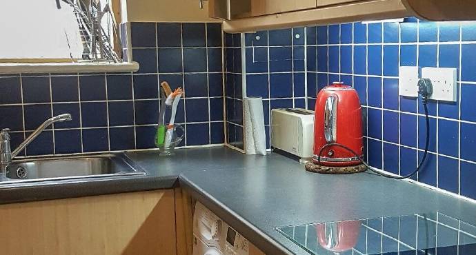 A woman in a blue shirt and gloves meticulously cleans a stove and extractor fan in a kitchen for end-of-tenancy cleaning.