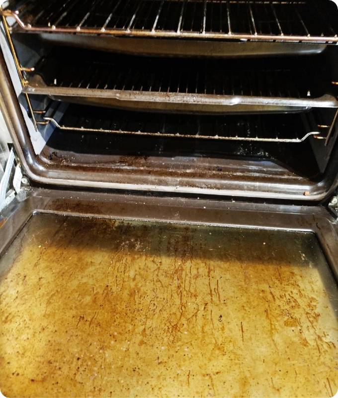 The image shows an open oven that is highly neglected, it is caked with grease and burnt black gunk.