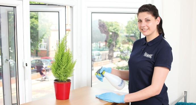 A regular cleaner in uniform who polishes a furniture.