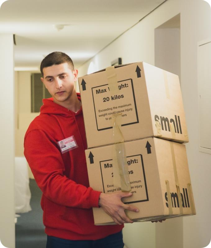The image shows a Fantastic Services mover who is carrying a couple of boxes filled with belongings and taking them out of a house.