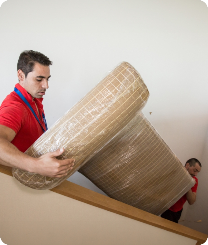 The image shows two Fantastic Services movers who are carrying an upholstered seat downstairs.