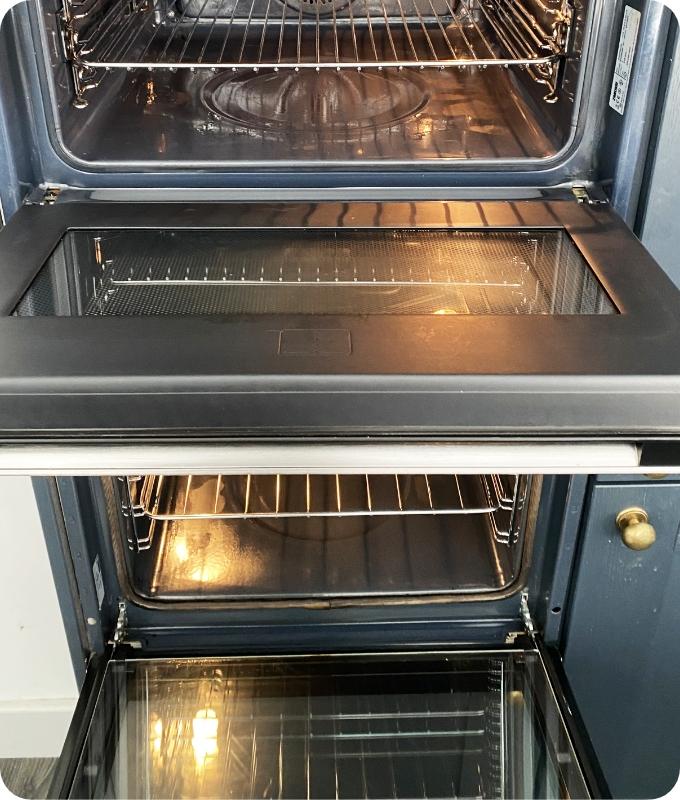 The image shows the same double oven after a thorough cleaning. All surfaces, both inside and outside, including oven racks and trays, appear perfectly clean and polished. The contrast is stark.