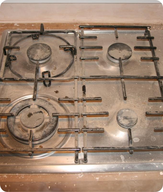 The image shows a gas stove that is heavily caked with stains and splatters from cooking.