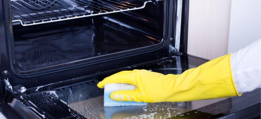 a professional cleaner's hand wearing a yellow protective glove cleaning the oven glass door from the inside