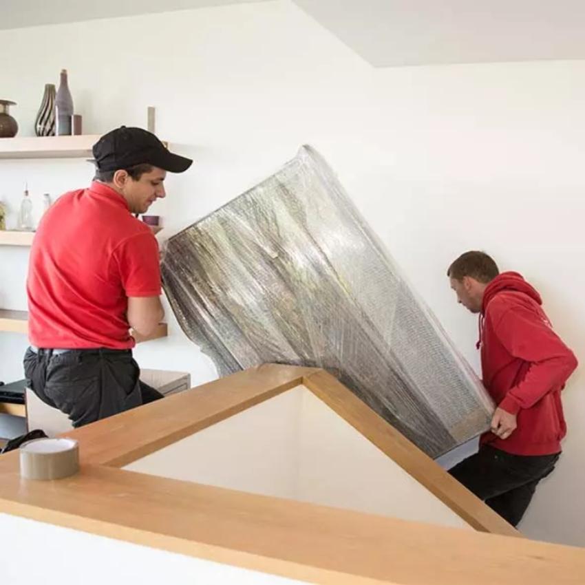 Two professional removalists moving packed furniture down the stairs of a property.