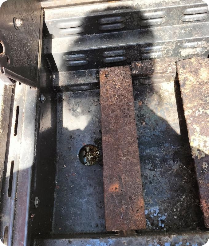 The image shows the inside of the bottom of a grill before professional cleaning service. It appears dirty and gunky.