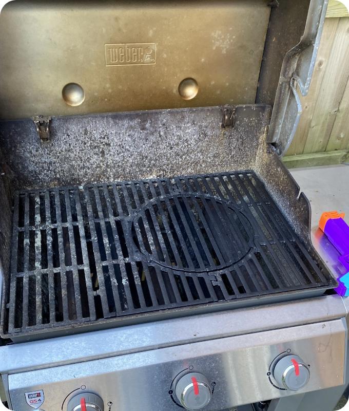 The image shows a grill that is quite dirty and neglected, with a filthy rack and lid.