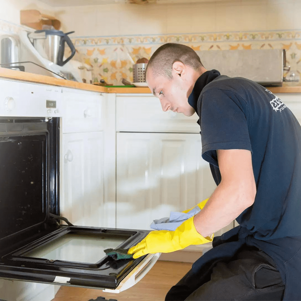 An oven technician in uniform is cleaning the oven glass from inside.