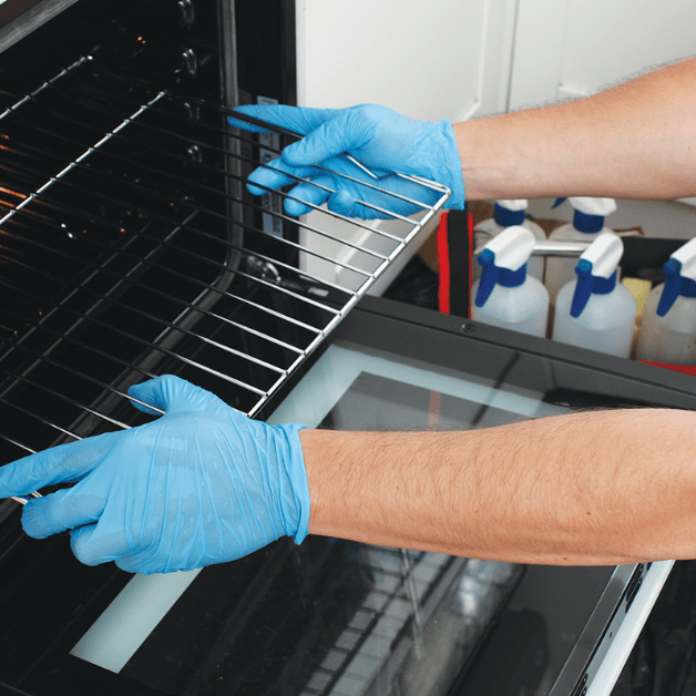 Close-up of a technician's hands inserting an oven rack into a freshly cleaned oven.