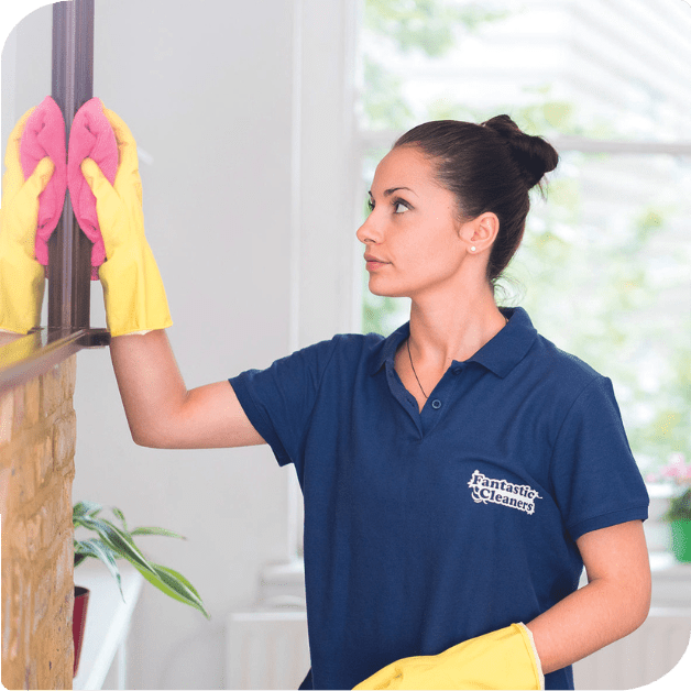 A woman in a blue shirt and yellow gloves is doing cleaning tasks in a kitchen.