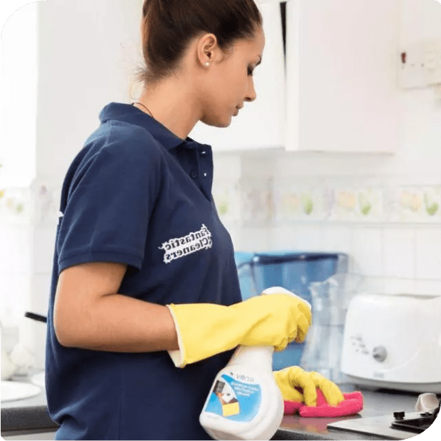 A woman in a blue shirt and yellow gloves is doing cleaning tasks in a kitchen.