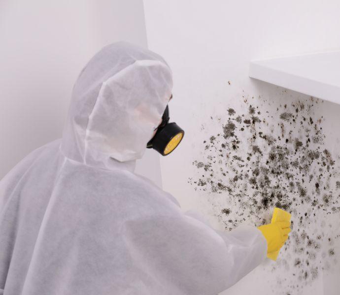 A professional with a protective suit and a gas mask scrubbing mould with a sponge